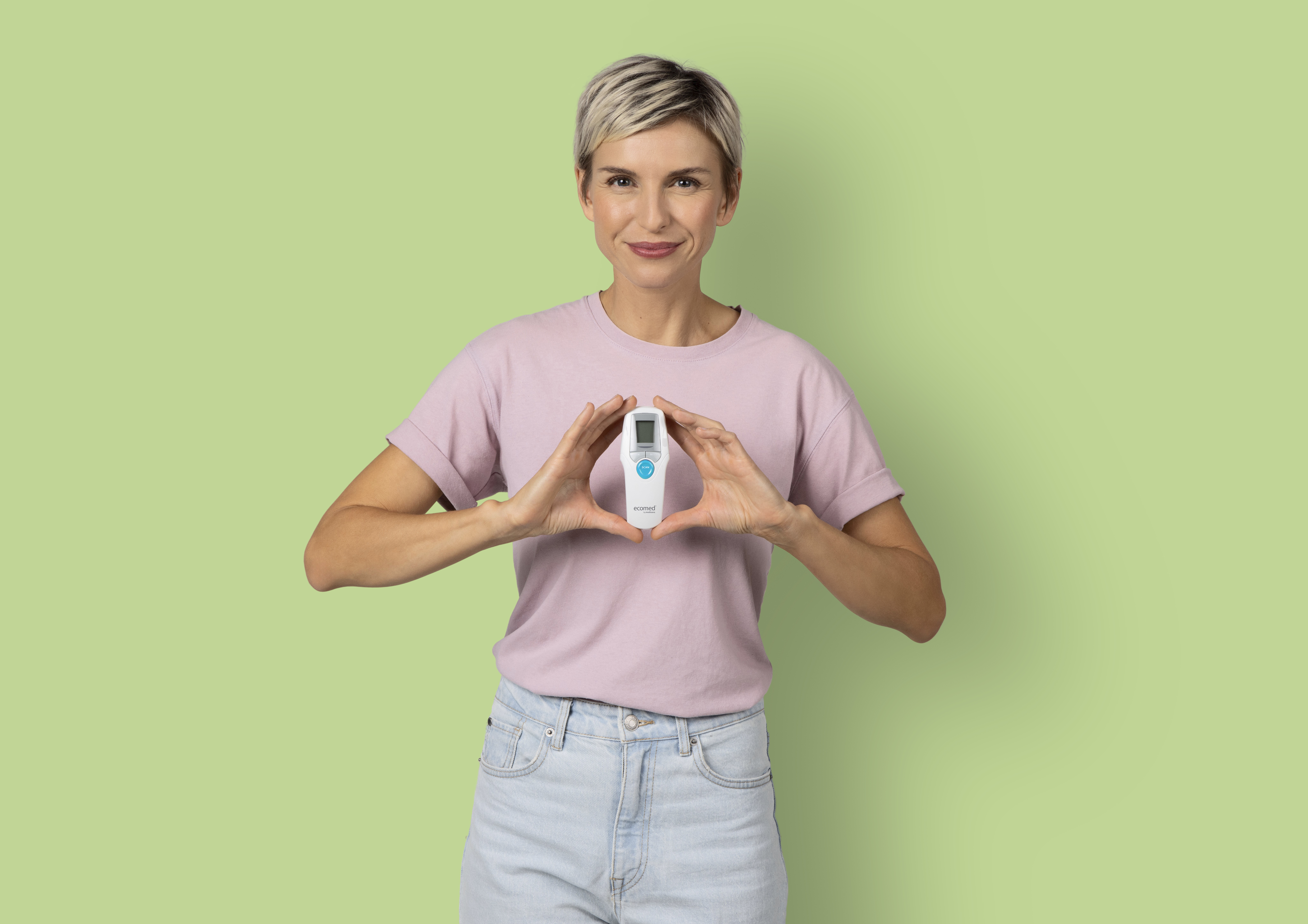 Woman holding a white thermometer, smiling. Green background. Shows a thermometer for temperature.