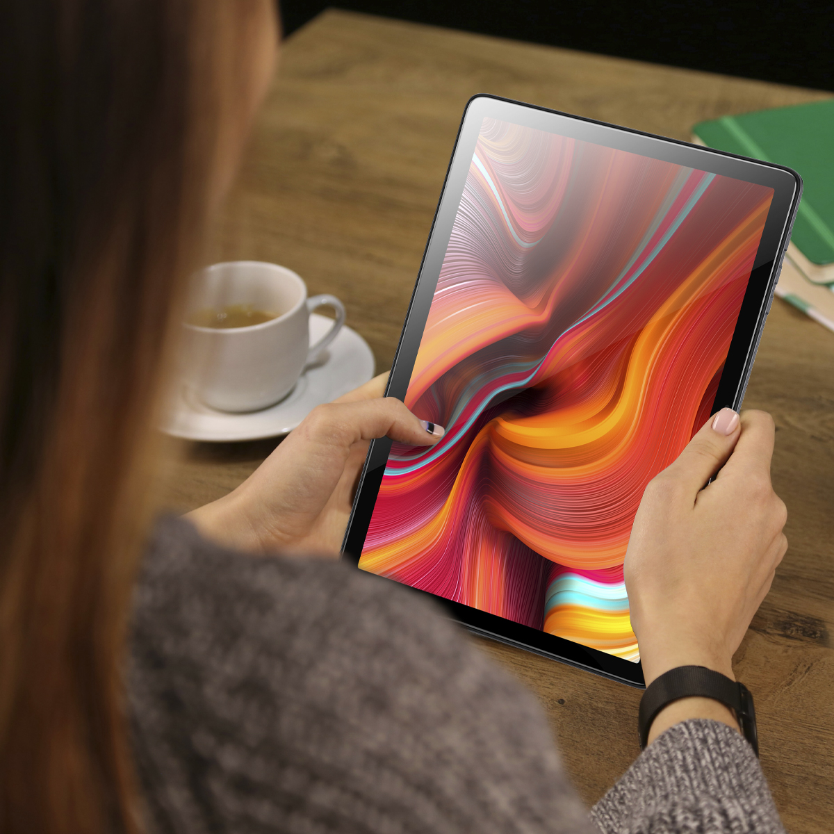 Kobieta trzyma tablet z kolorową sztuką abstrakcyjną na drewnianym stole.