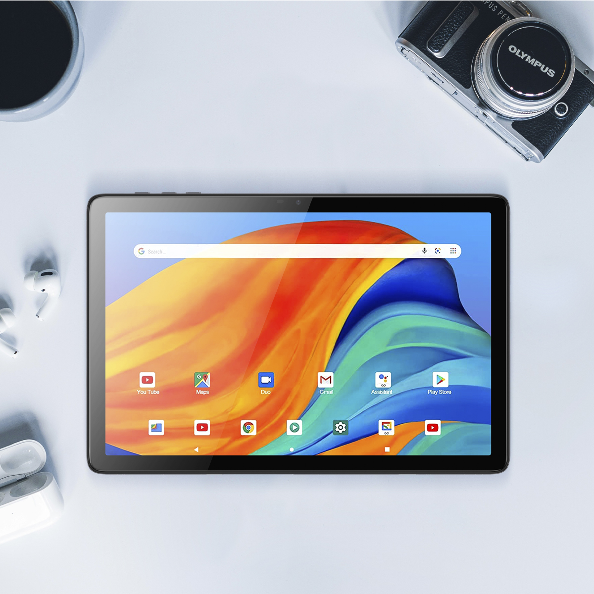 Tablet z kolorowym ekranem wyświetlającym ikony aplikacji oraz aparat i słuchawki na stole.