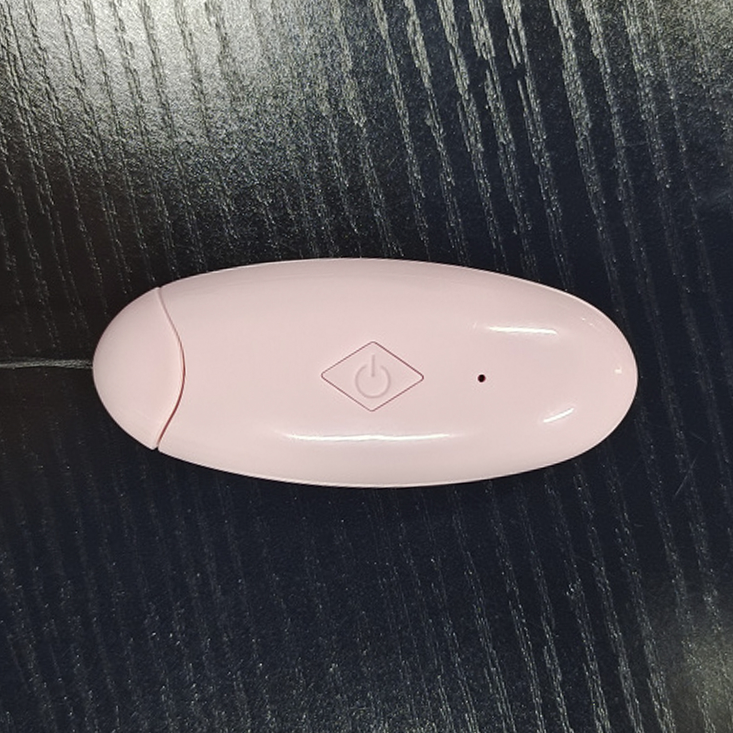 Dispositivo rosa ovalado con un icono de botón de encendido sobre una superficie de madera oscura.