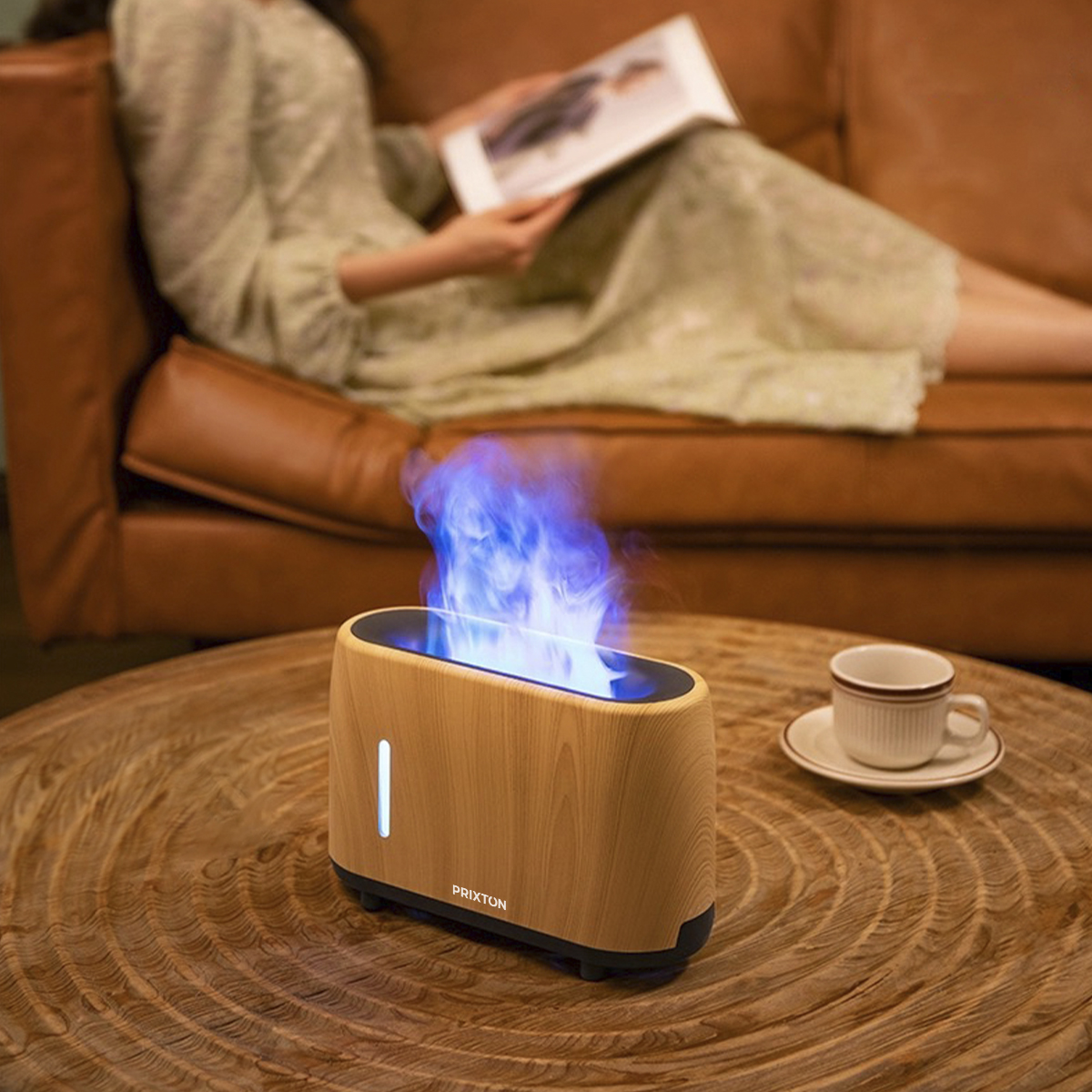 Un difusor de aroma estilo madera con niebla azul. Una persona lee un libro en un sofá de cuero marrón.