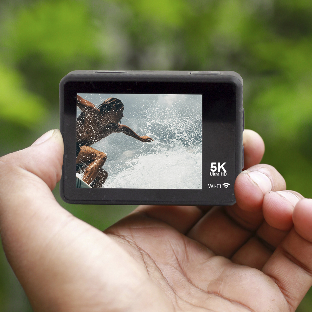 Dłoń trzymająca czarną kamerę sportową. Kamera pokazuje surfera na fali, 5K Ultra HD.