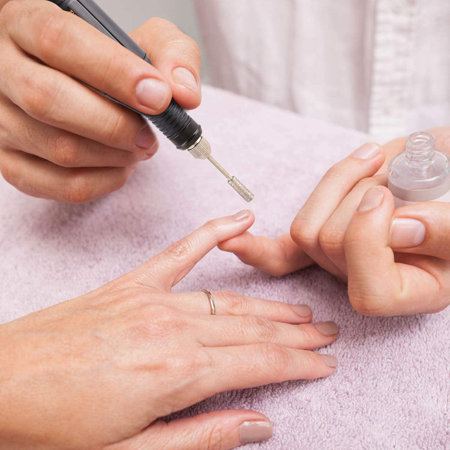 Ręce wykonujące manicure. Frezarka do paznokci jest używana na paznokciu, obok butelka lakieru do paznokci.