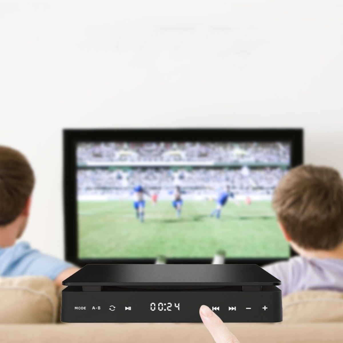 Schwarzer Mediaplayer auf einem Tisch mit einem Fernseher, der ein Fußballspiel zeigt.