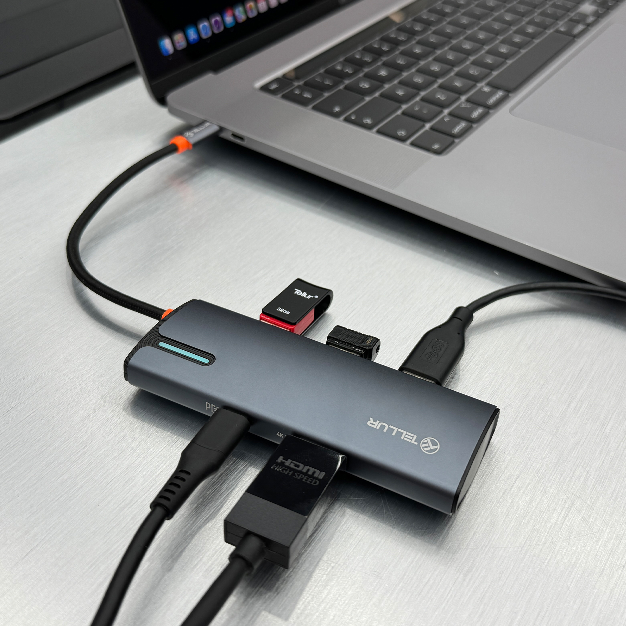 Srebrny hub z wieloma portami jest podłączony do laptopa. Do huba podłączonych jest kilka kabli.