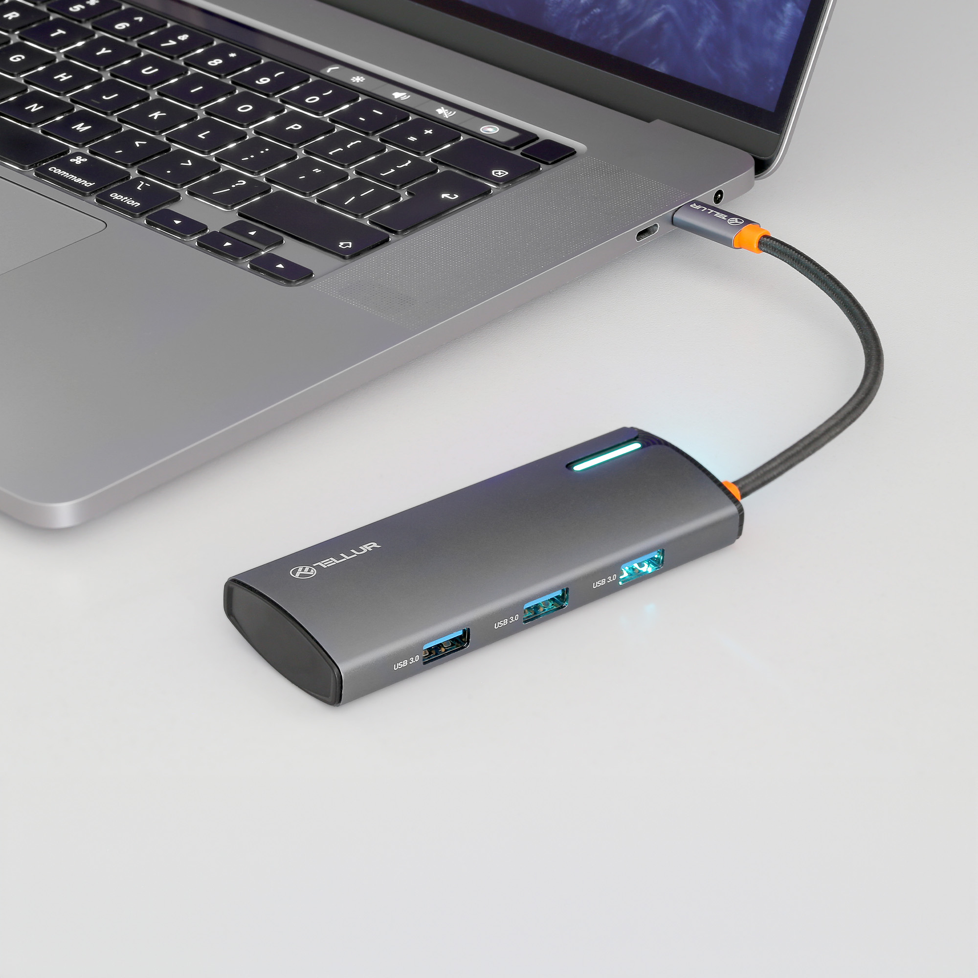 Laptop podłączony do huba USB Tellur. Hub jest szary z niebieskimi światłami i portami USB.