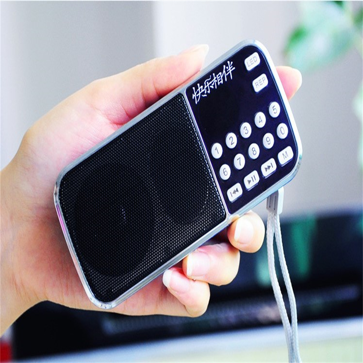 Eine Hand hält ein kleines, schwarz-silbernes Radio mit Knöpfen und einem Lautsprecher.