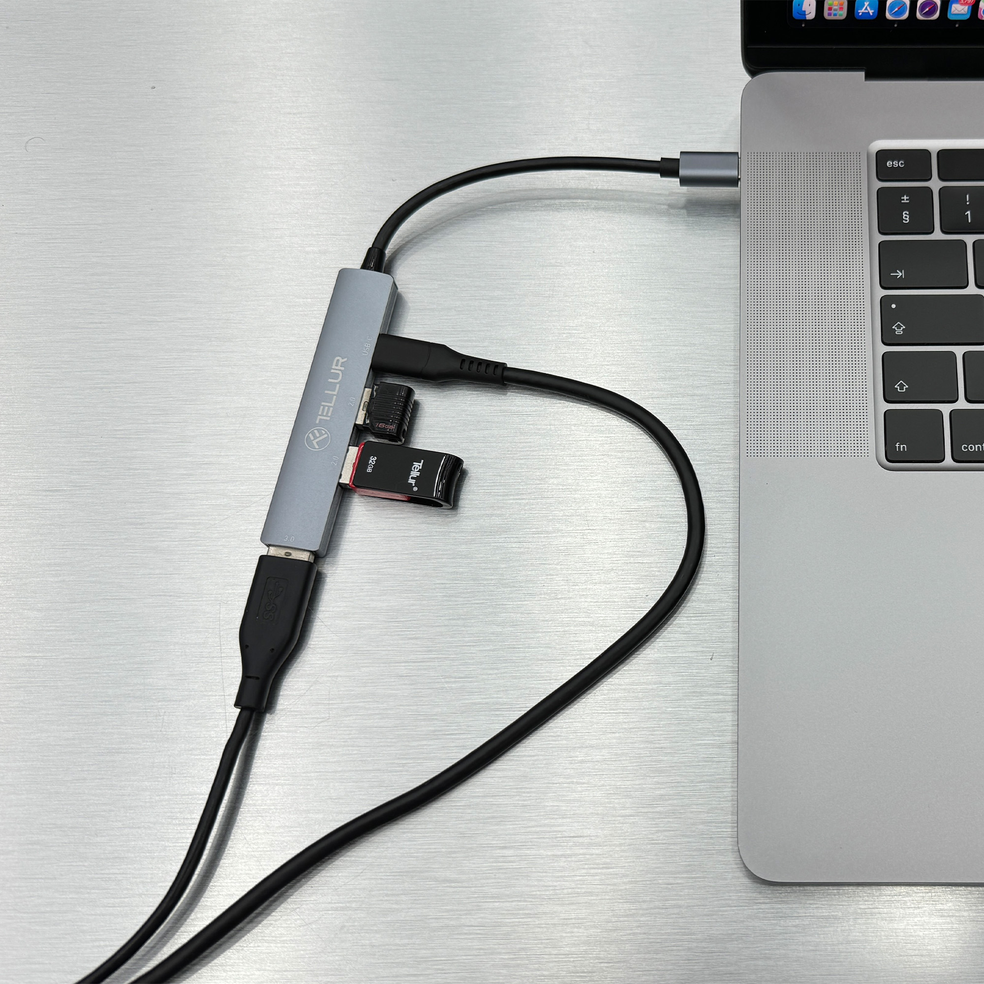 Laptop podłączony do szarego huba z wieloma dyskami USB i kablami.