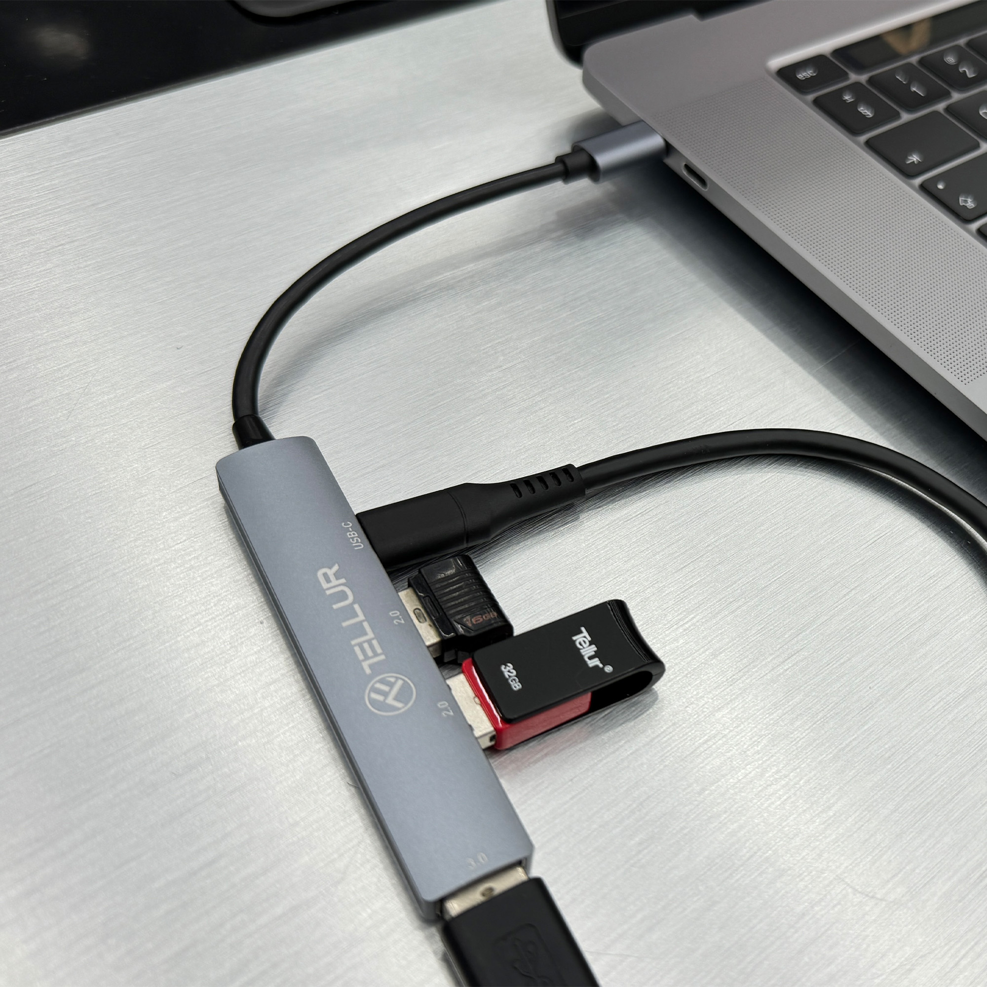 Hub USB-C z dyskami USB podłączonymi do laptopa na metalowej powierzchni.
