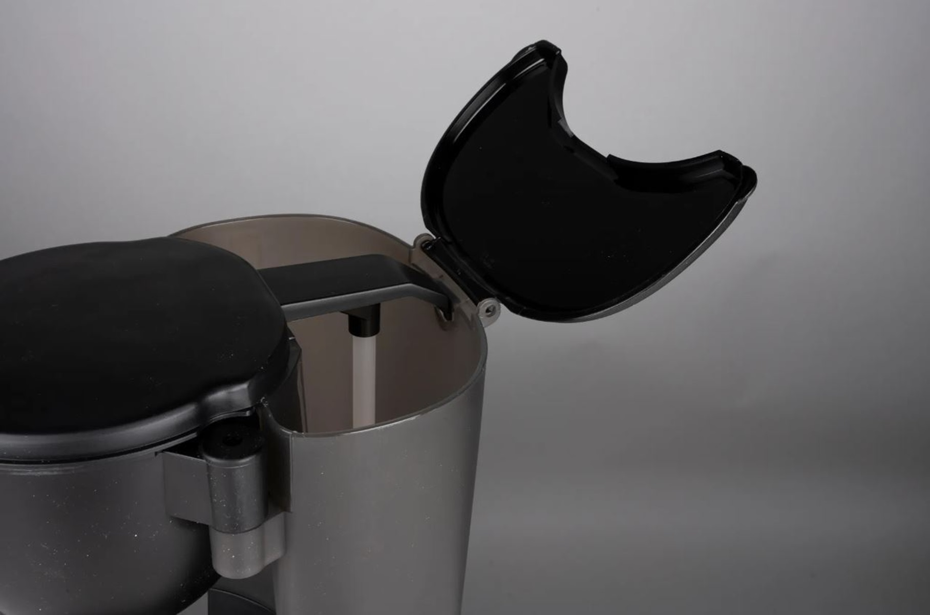 Nahaufnahme einer grau-schwarzen Kaffeemaschine mit geöffnetem Deckel, der das Innere freigibt.