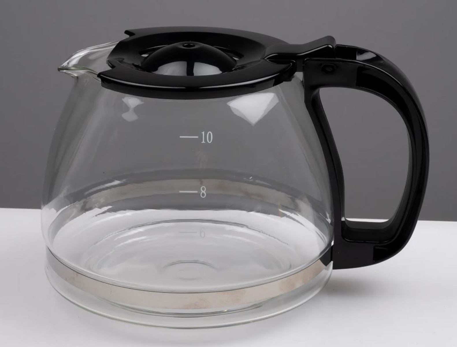 Eine Kaffeekanne aus klarem Glas mit schwarzem Deckel und Griff. Sie hat Volumenmarkierungen. Grauer und weißer Hintergrund.