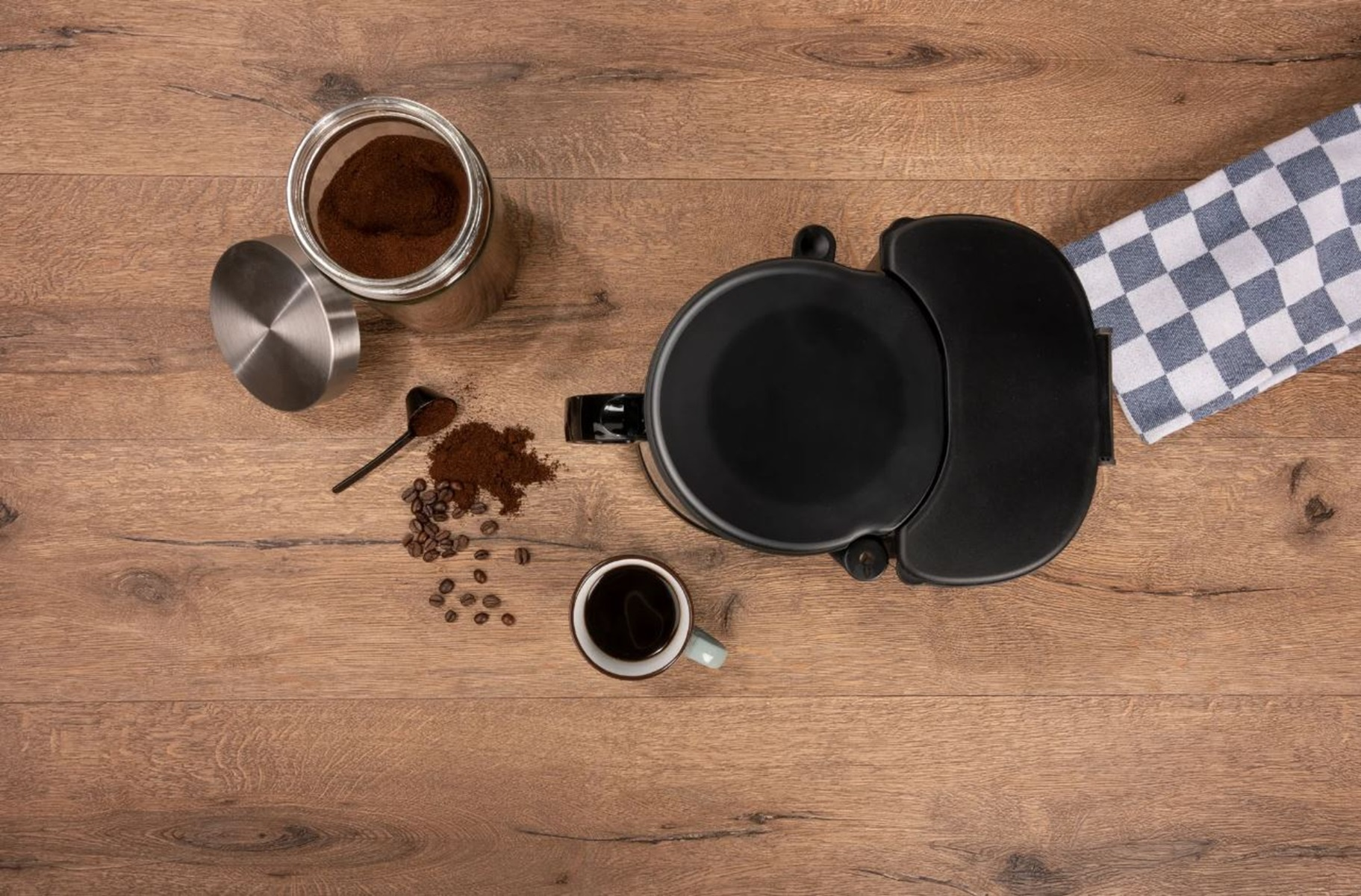 Kaffeebezogene Artikel, darunter eine Kaffeemaschine, Kaffeebohnen und eine Tasse auf Holz.