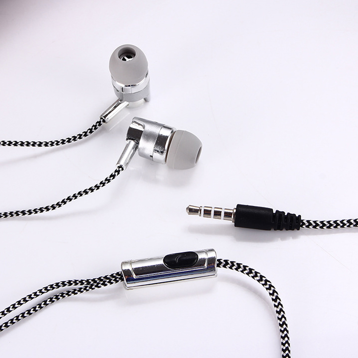 Ein Paar silberne und graue Ohrhörer mit einem Controller und einem schwarz-weißen geflochtenen Kabel auf weißer Oberfläche.