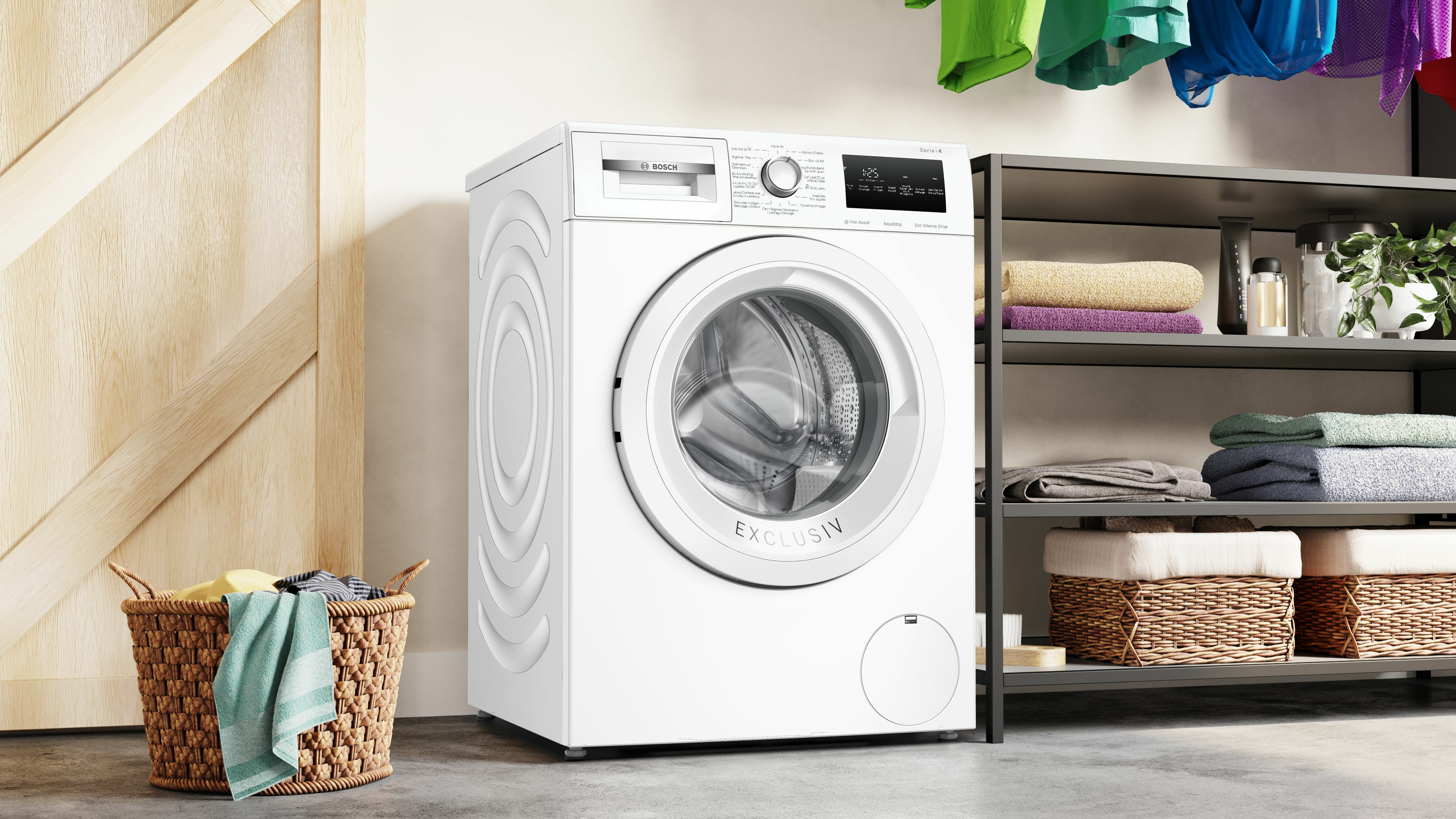 Weiße Bosch Waschmaschine. Wäschekorb mit Kleidung links. Trocknende Kleidung im Hintergrund.