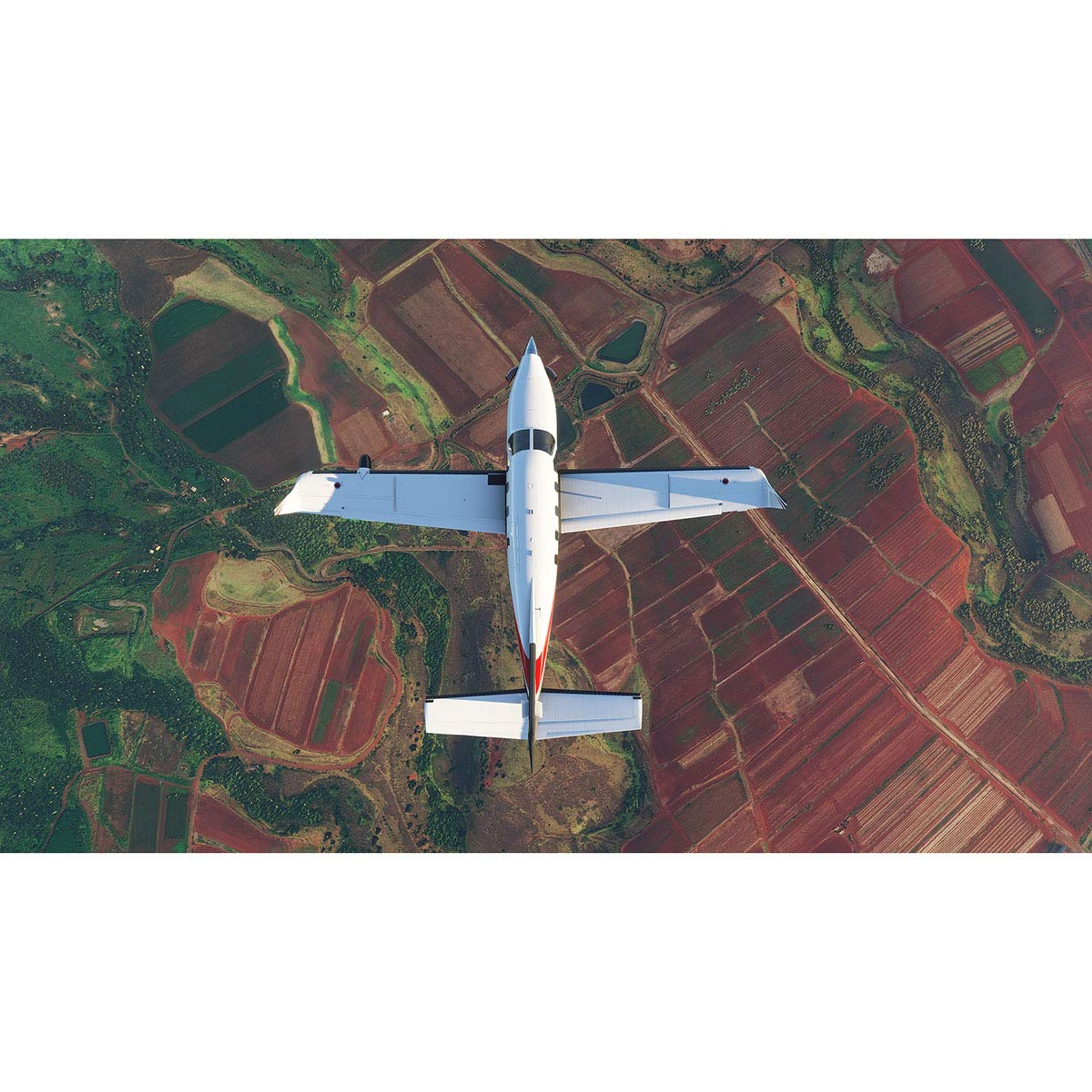Draufsicht auf ein weißes Flugzeug, das über Felder mit roten und grünen Mustern fliegt.