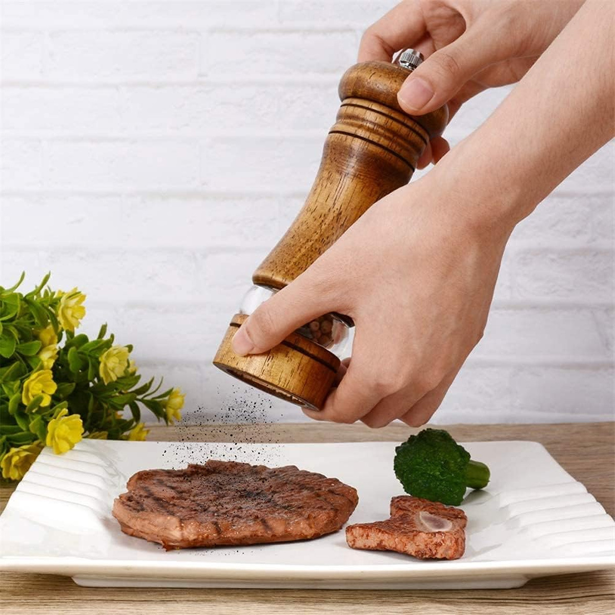 Hände mahlen Pfeffer auf Steak, Brokkoli auf weißem Teller.