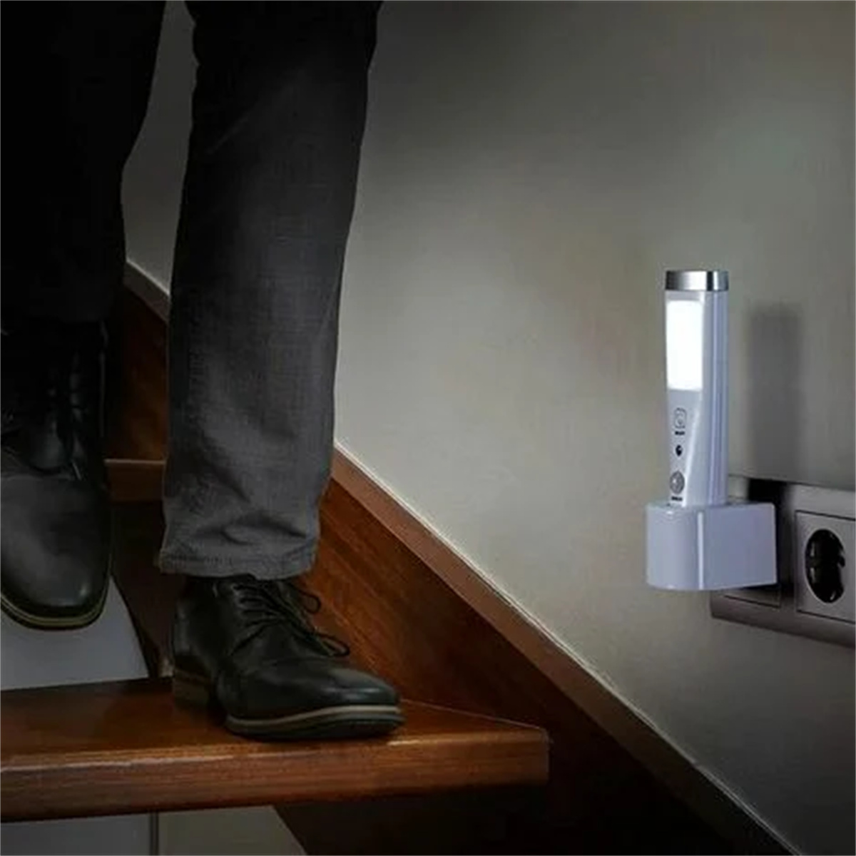 Eine Person auf einer Treppe, in der Nähe einer Wand mit einem eingesteckten Nachtlicht. Das Licht ist weiß.