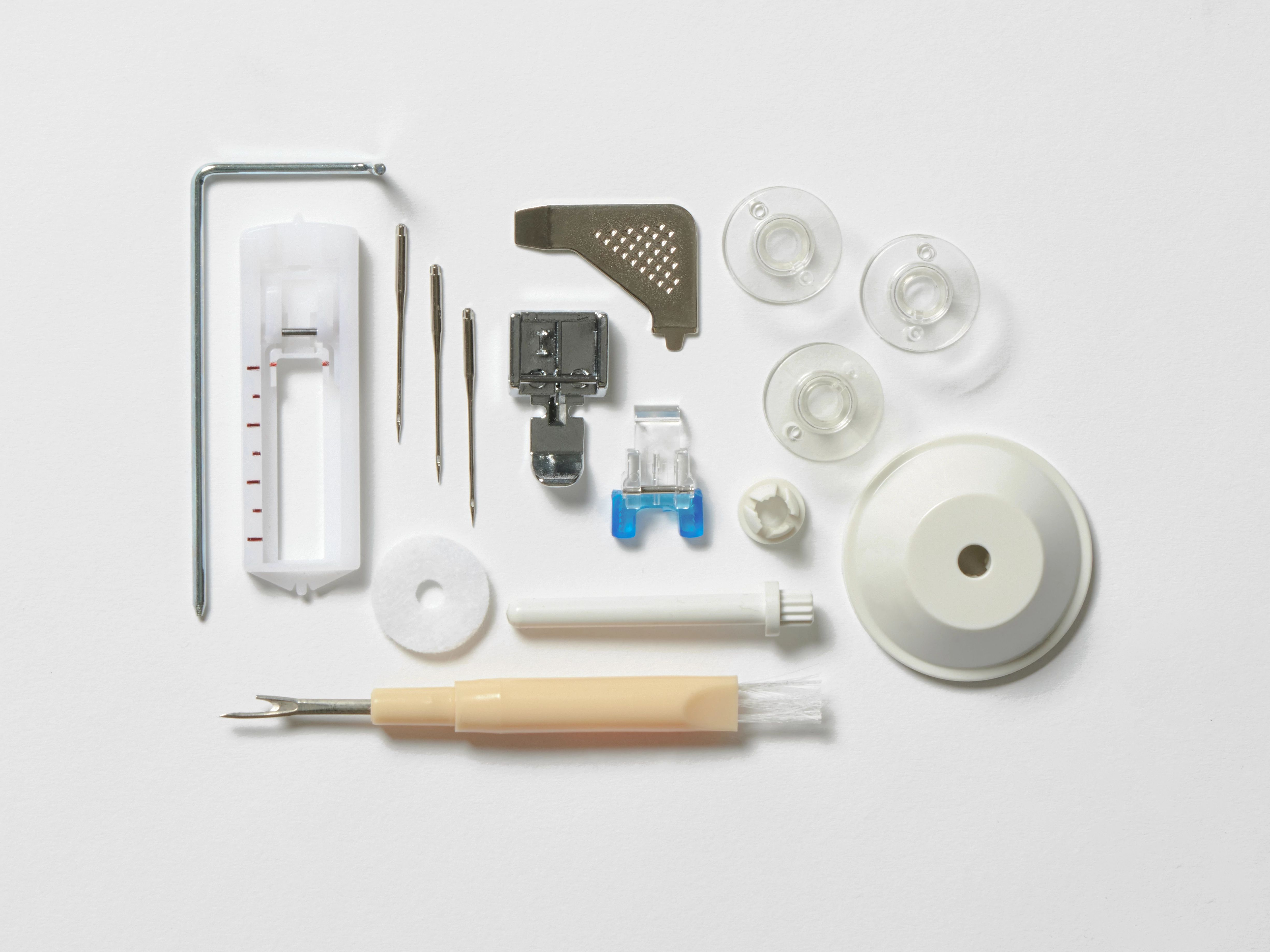 Accesorios de máquina de coser sobre superficie blanca: prensatelas, agujas, bobinas y un abreojales.