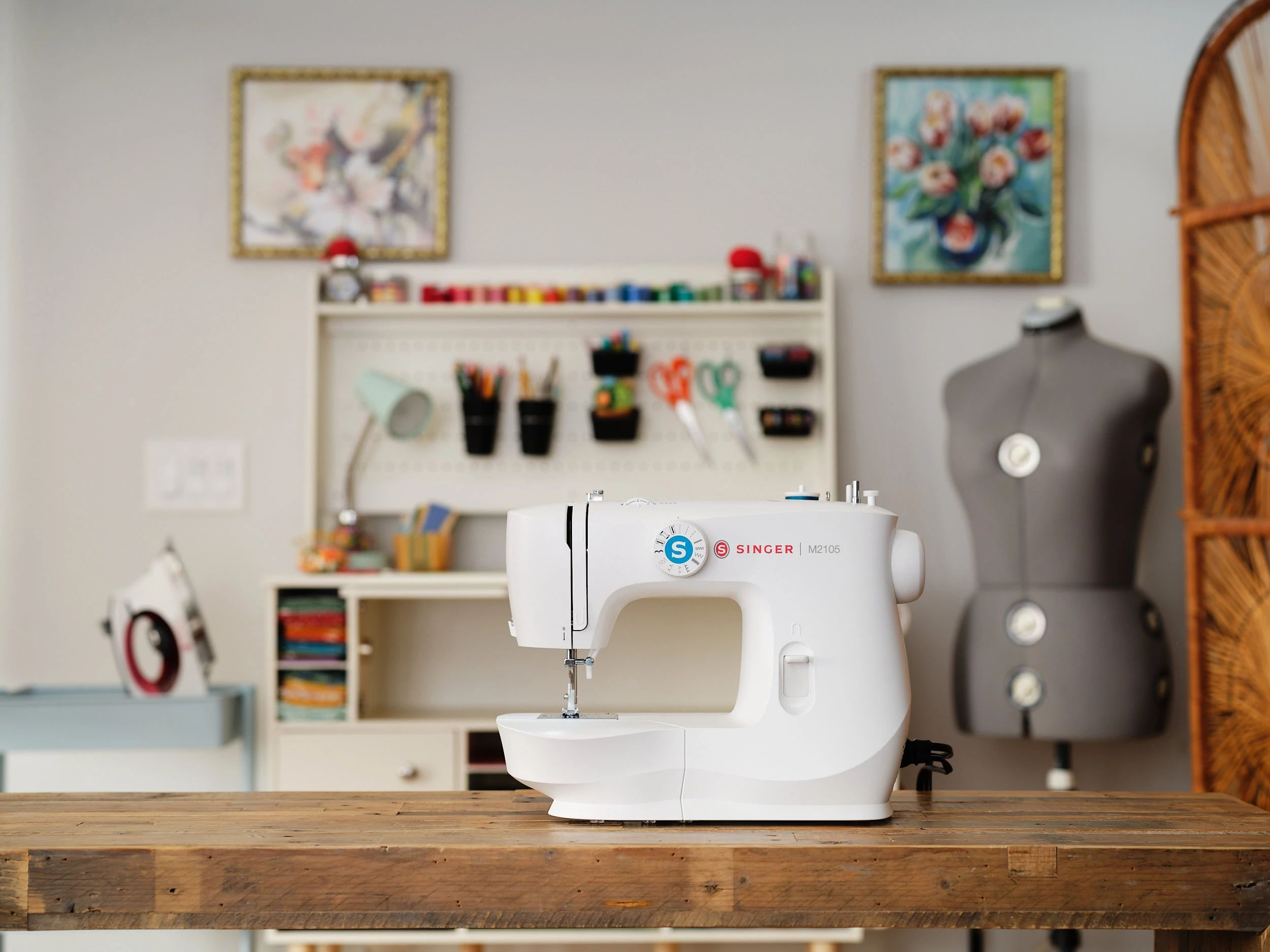 Biała maszyna do szycia Singer na drewnianym stole. Manekin i sztuka w tle.