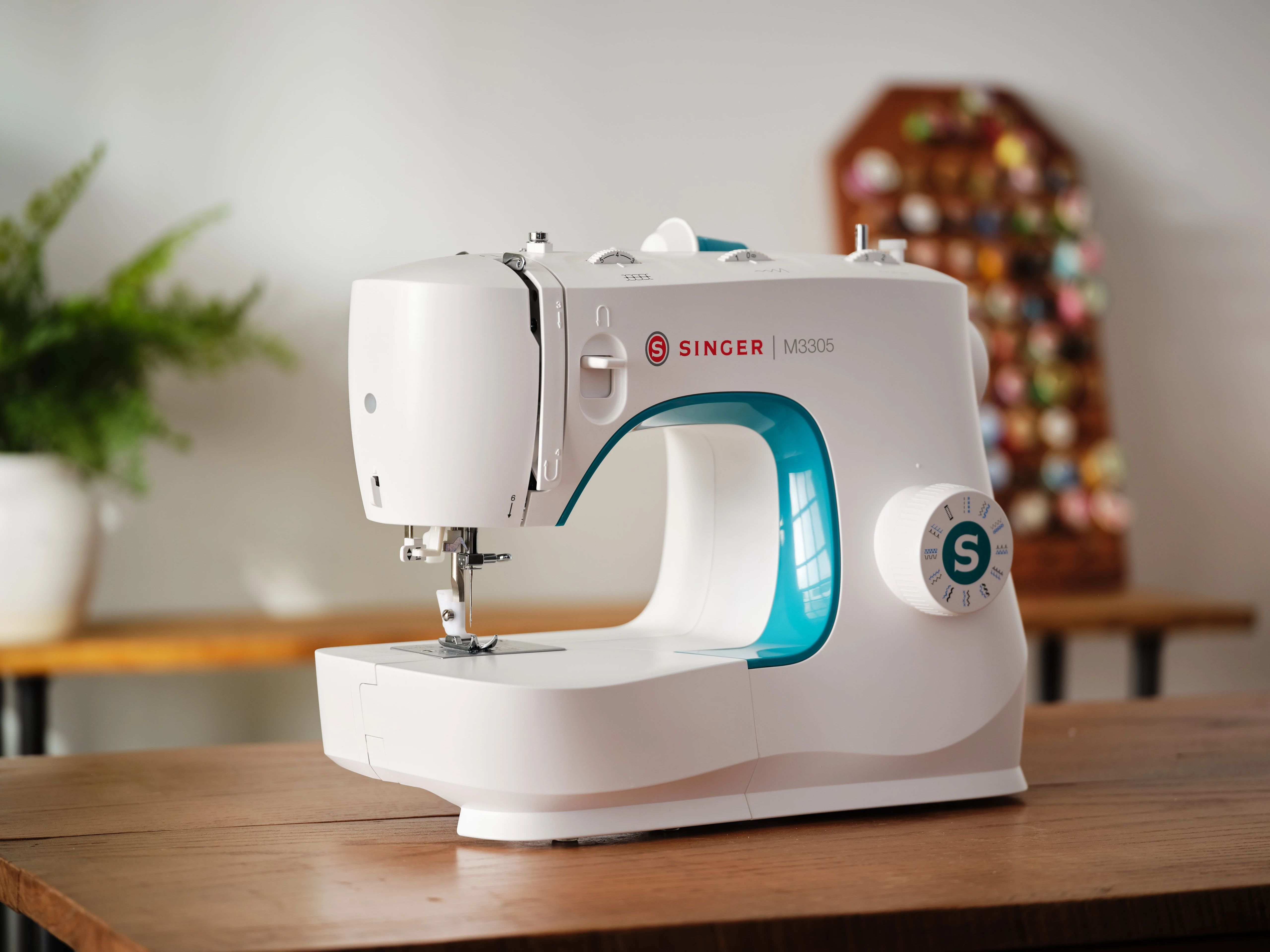Biała maszyna do szycia Singer z turkusowymi akcentami, na drewnianym stole.