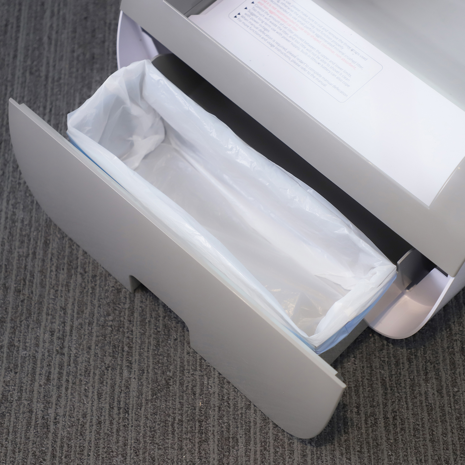 Geöffnete Mülleimer-Schublade mit Plastiktüte, positioniert in einem größeren grauen Gerät.