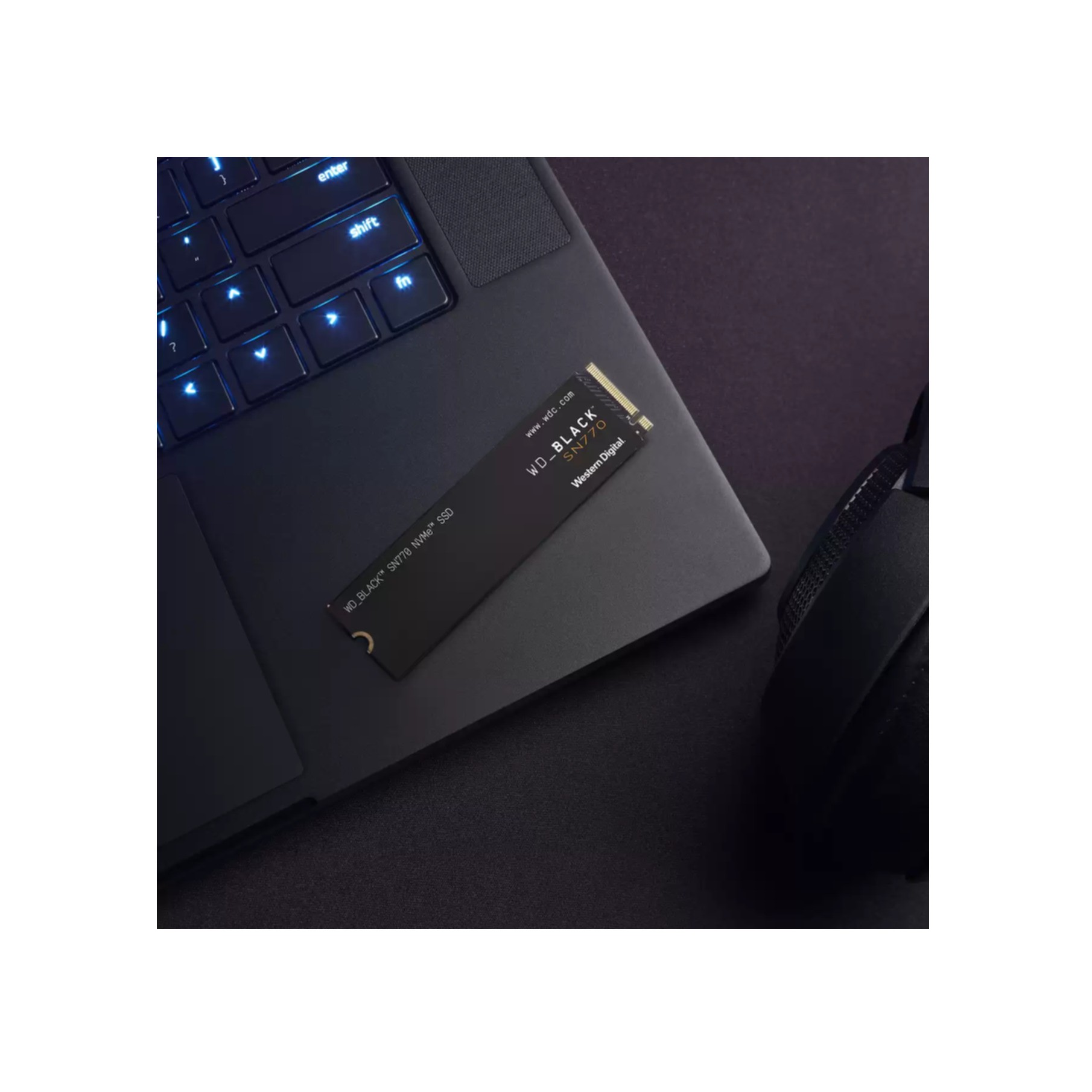 SSD sur un ordinateur portable. L'ordinateur portable est sur une surface sombre, avec un casque et un clavier dans le cadre.