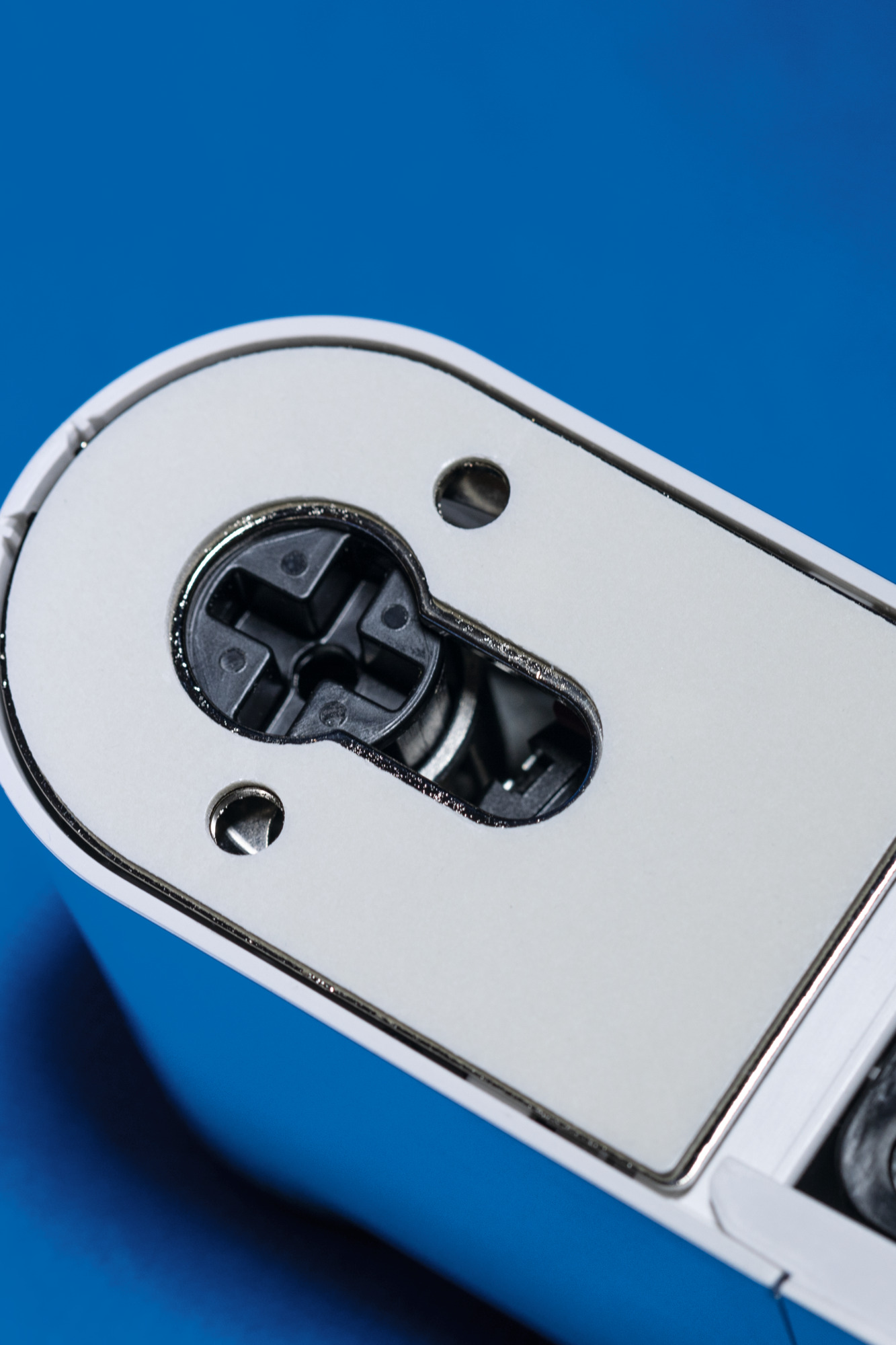 Zbliżenie na dziurkę od klucza. Widoczna biała powierzchnia z czarną dziurką od klucza w kształcie krzyża. Niebieskie tło.