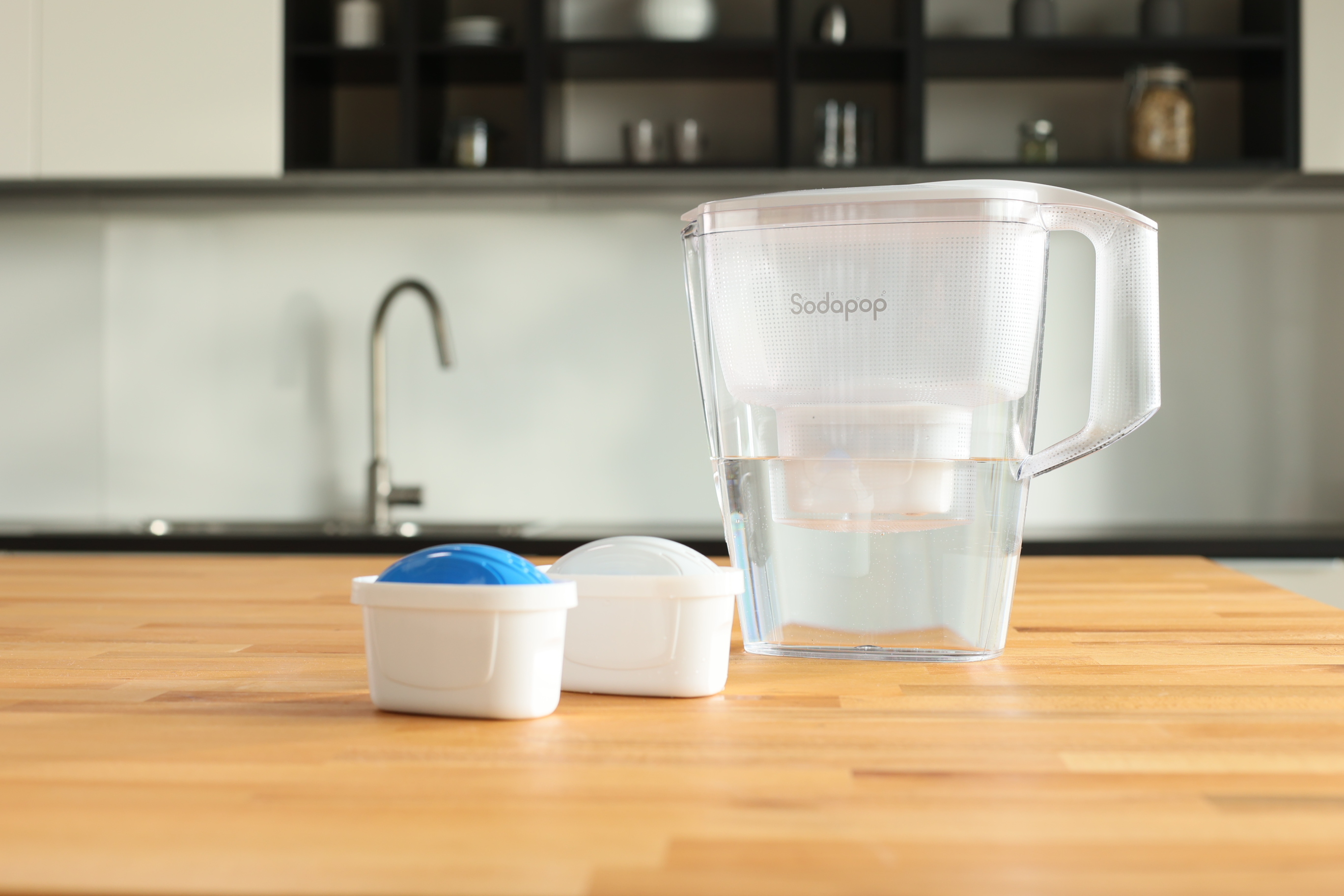 Brocca filtrante con filtri e acqua, su un piano di lavoro in legno in cucina.