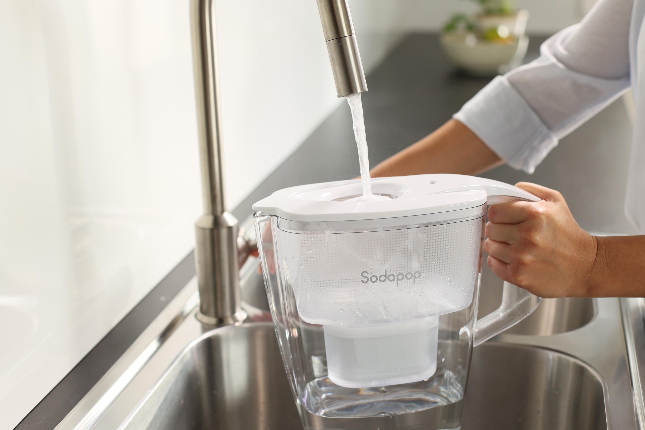 Una persona riempie una brocca con filtro d'acqua con acqua dal rubinetto in una cucina.