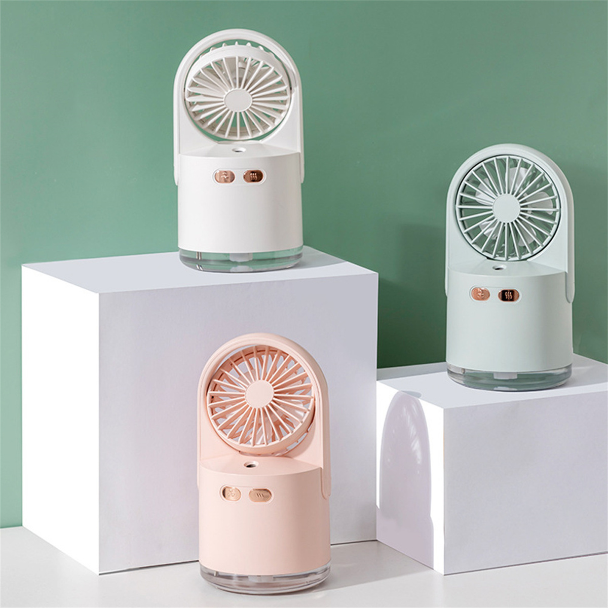 Drei kleine Ventilatoren in Weiß, Türkis und Rosa, auf weißen Blöcken, grüner Hintergrund.