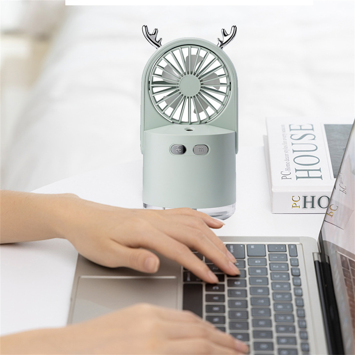 Kleiner mintgrüner Ventilator mit Hirschgeweih oben. Hände einer Person sind auf einer Laptop-Tastatur.