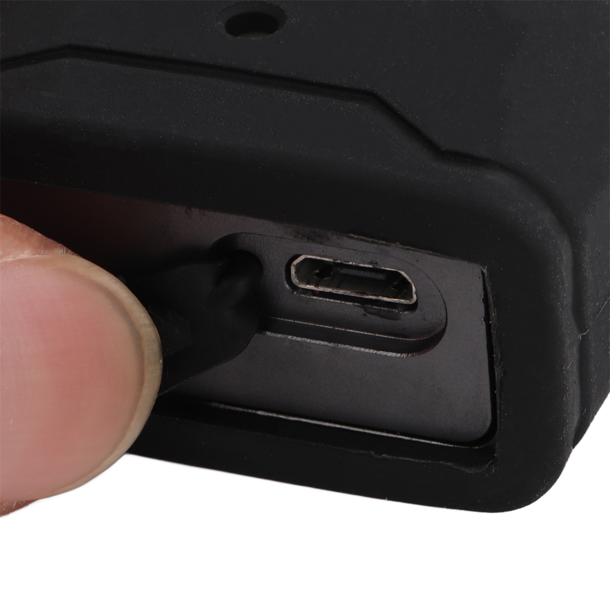 Nahaufnahme eines schwarzen Geräts mit Ladeanschluss, wobei ein Finger ein schwarzes Kabel einführt.
