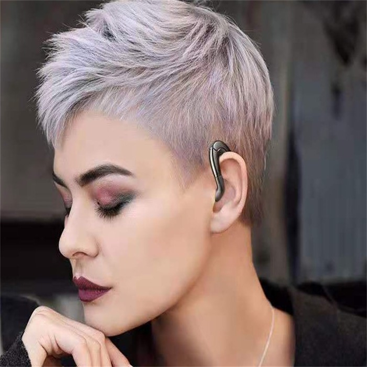 Eine Frau mit kurzen grauen Haaren, die einen schwarzen Ohrhörer trägt, Nahaufnahme, neutraler Hintergrund.