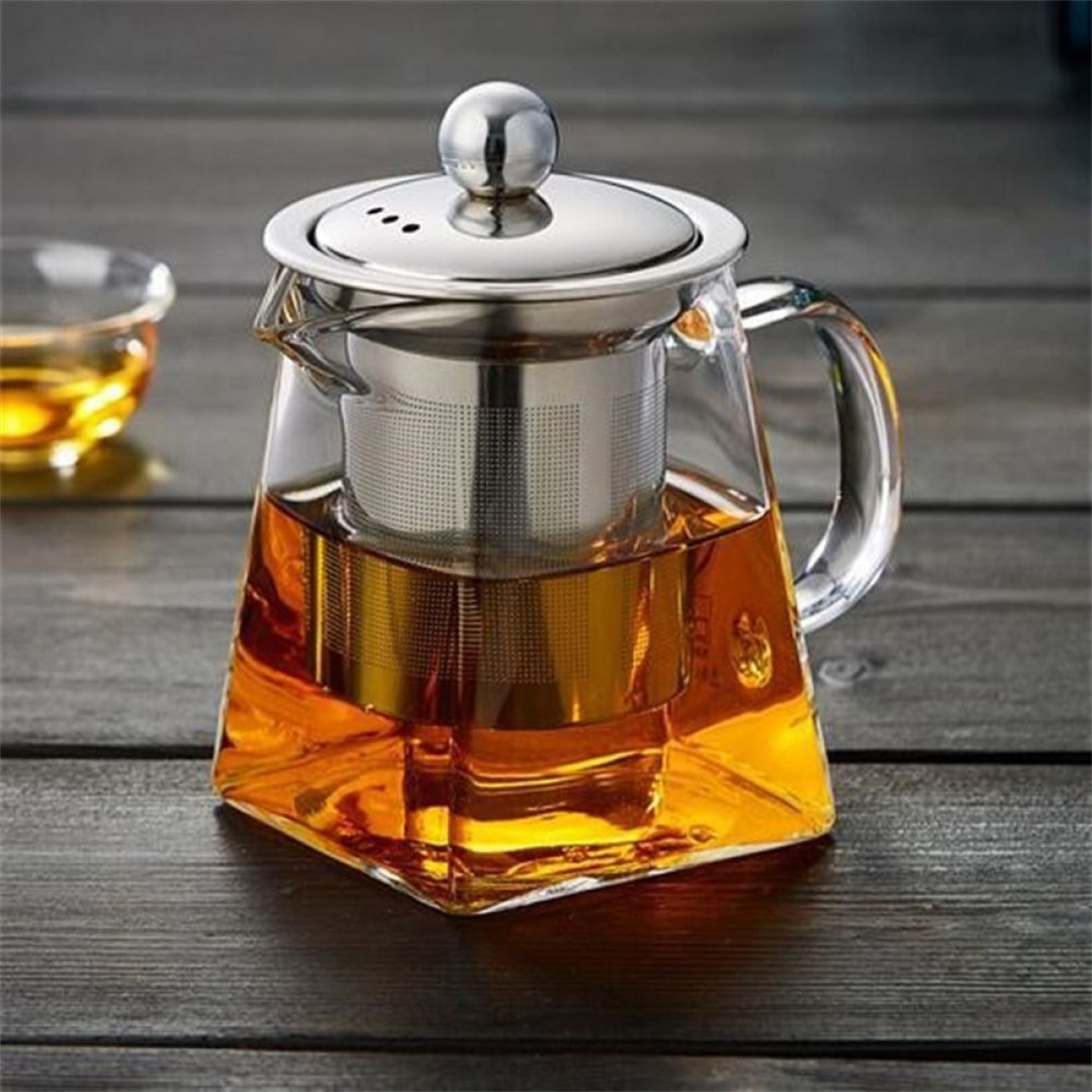 Glaskanne mit Tee und Edelstahl-Infuser. Kanne steht auf einem Holztisch.
