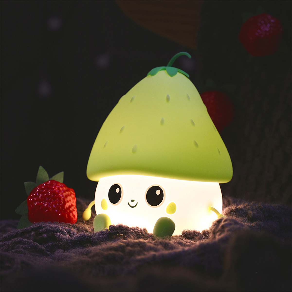 Ein erdbeerförmiges Nachtlicht mit einem lächelnden Gesicht, auf dunklem Hintergrund mit Erdbeeren.