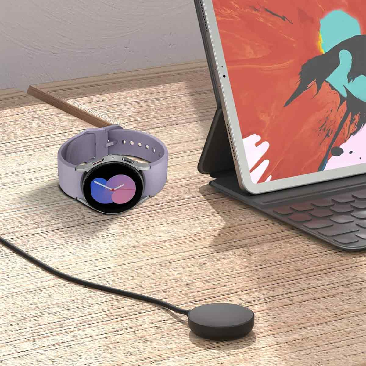 Eine lila Smartwatch und ein Ladepad mit schwarzem Kabel. Ein Tablet ist im Hintergrund geöffnet.