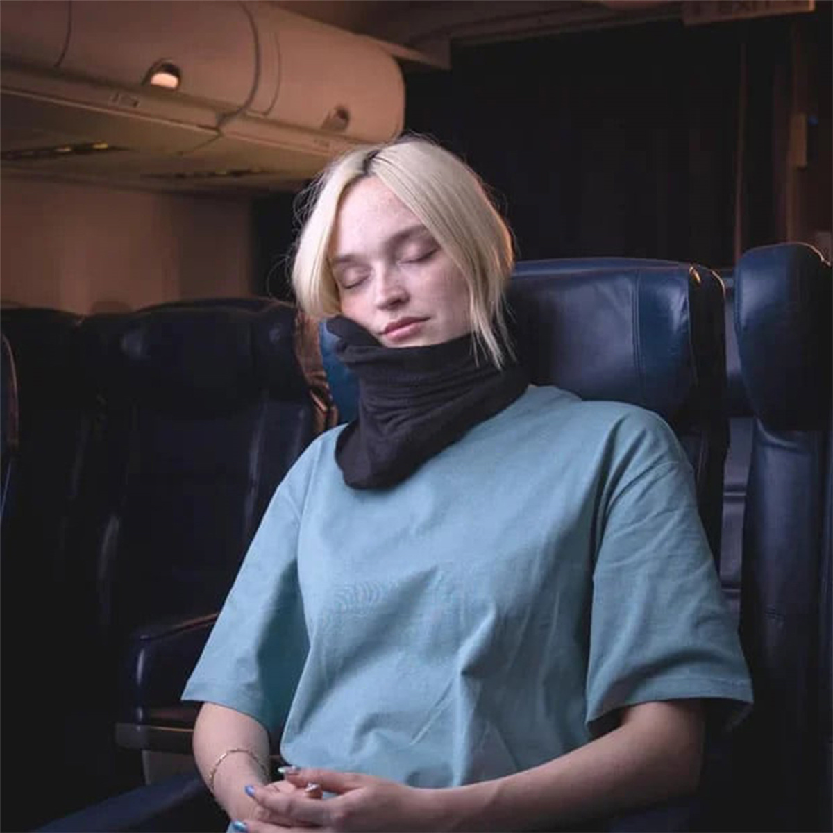 Eine blonde Frau schläft in einem Flugzeug mit einem Nackenkissen.