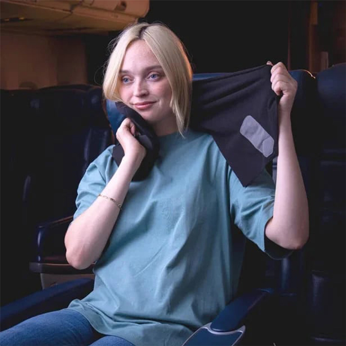 Eine Frau im Flugzeug mit einem Reisekissen um den Hals. Sie lächelt.
