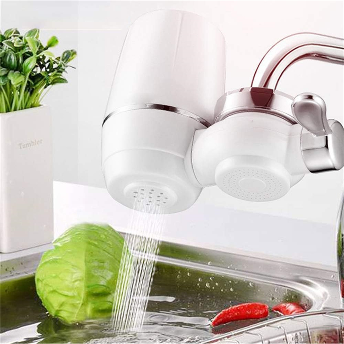 Ein weißer Wasserfilter an einem Wasserhahn, Wasser fließt in ein Waschbecken. Kohl und Paprika sind sichtbar.
