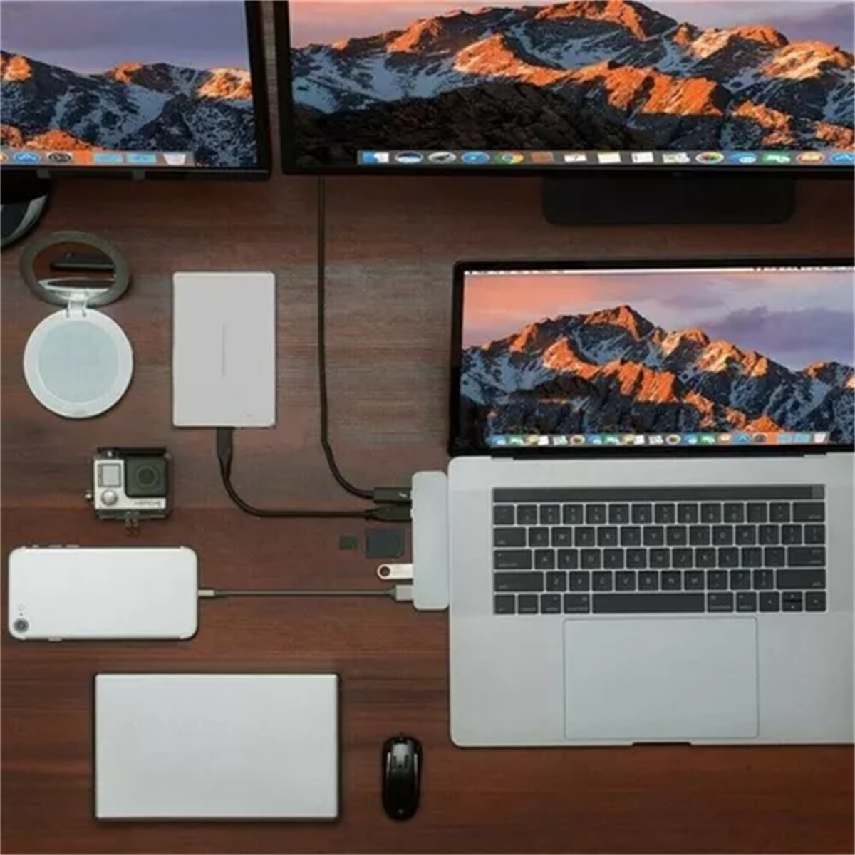 Schreibtisch mit Laptop und Zubehör. Spiegel, Kamera und verschiedene Geräte liegen darauf.