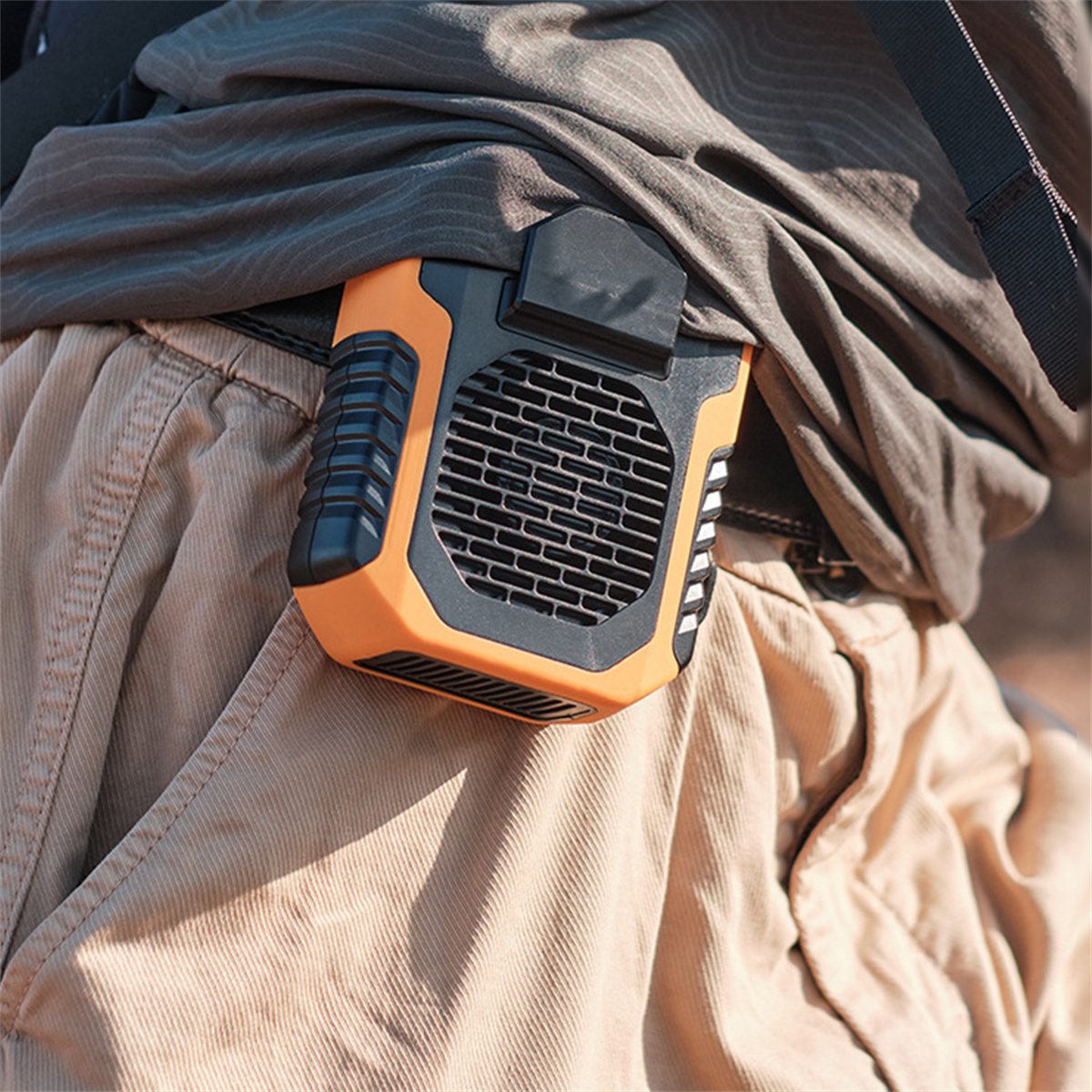 Ein orangefarbener und schwarzer tragbarer Ventilator, der an einem Gürtel befestigt ist. Der Ventilator hat ein schwarzes Gitter.