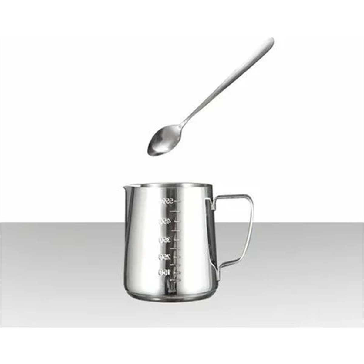 Eine Edelstahl-Milchkanne mit Messungen und ein Löffel darüber auf hellem Hintergrund.