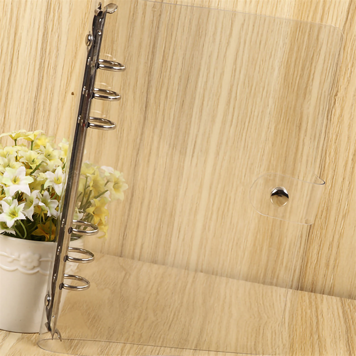 Transparenter Ordner mit silbernen Ringen. Gelbe Blumen im Hintergrund.