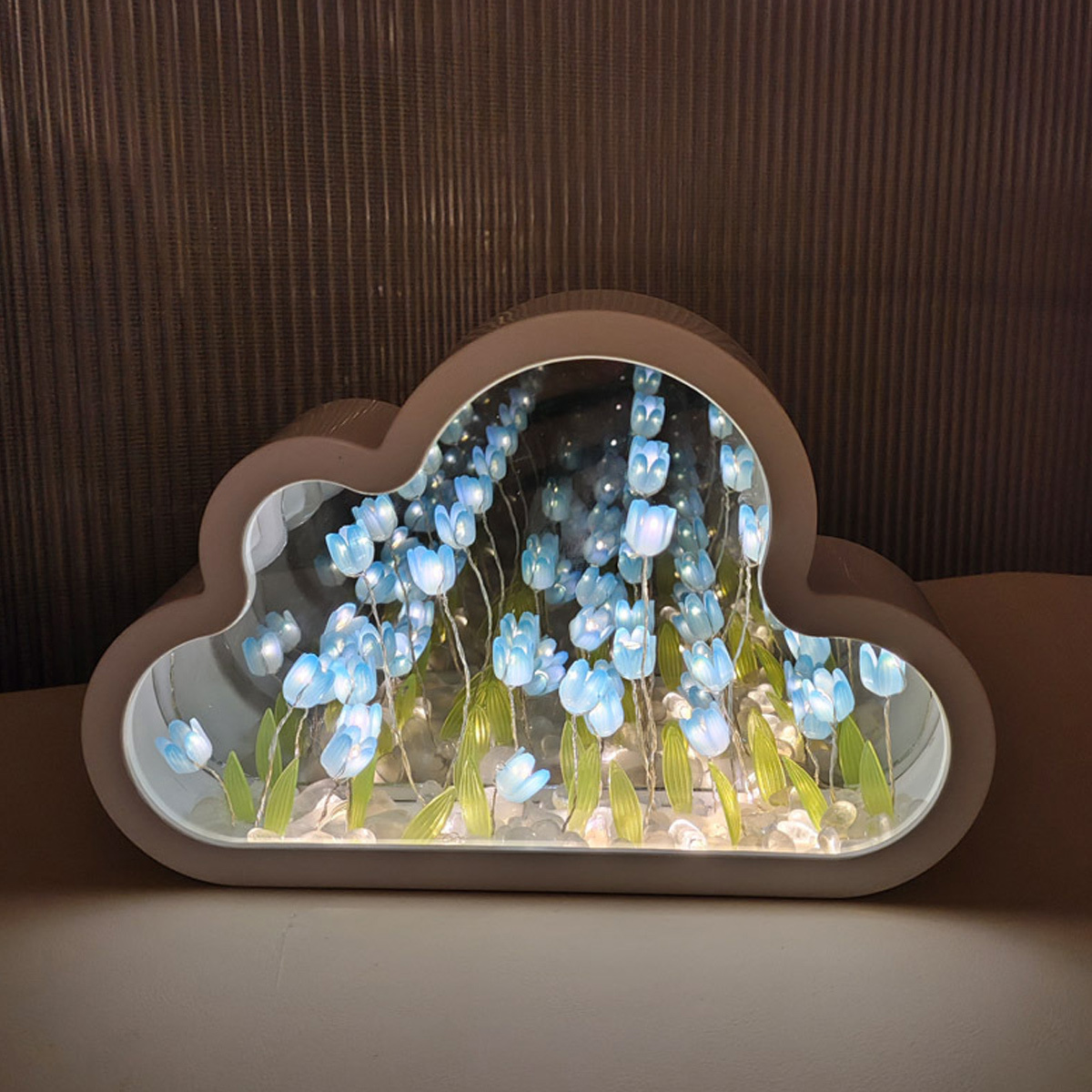 Wolkenförmige Leuchtbox mit blauen Blumendekorationen. Der Hintergrund ist eine dunkelbraune Wand.