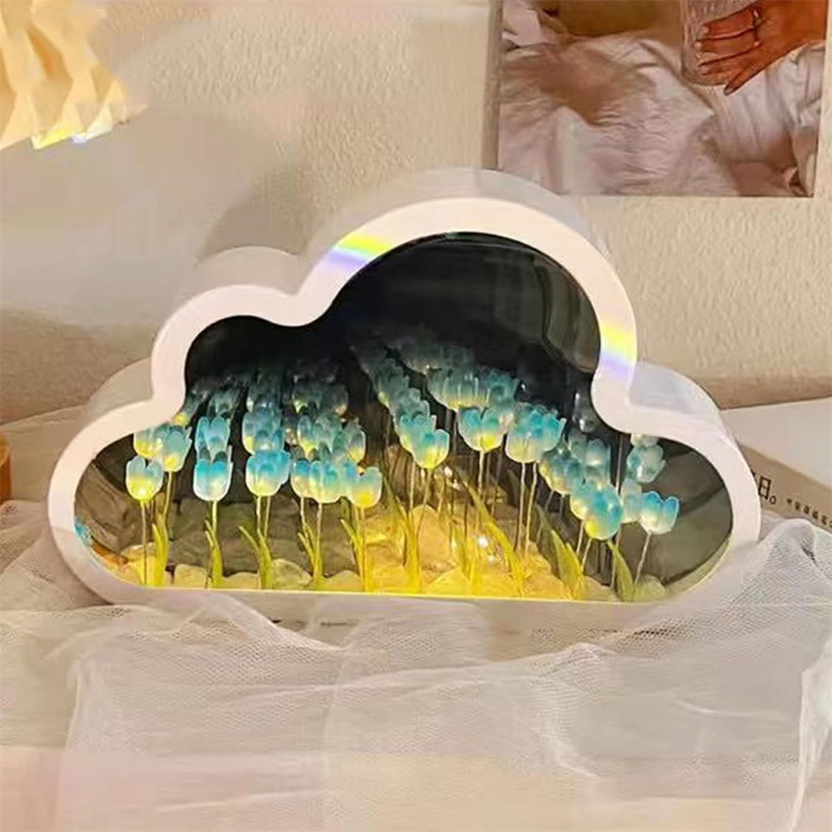 Wolkenförmiges Licht mit blauen Tulpen im Inneren. Das Licht steht auf einer weißen Oberfläche. Ein Bett ist im Hintergrund.