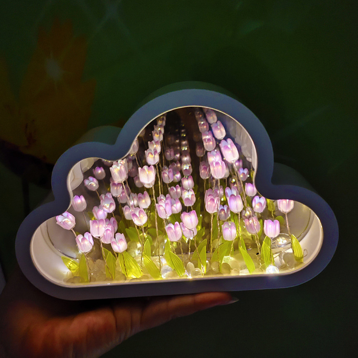 Wolkenförmige Leuchtbox mit floralem Arrangement im Inneren, sanft leuchtend. Hand, die es hält.