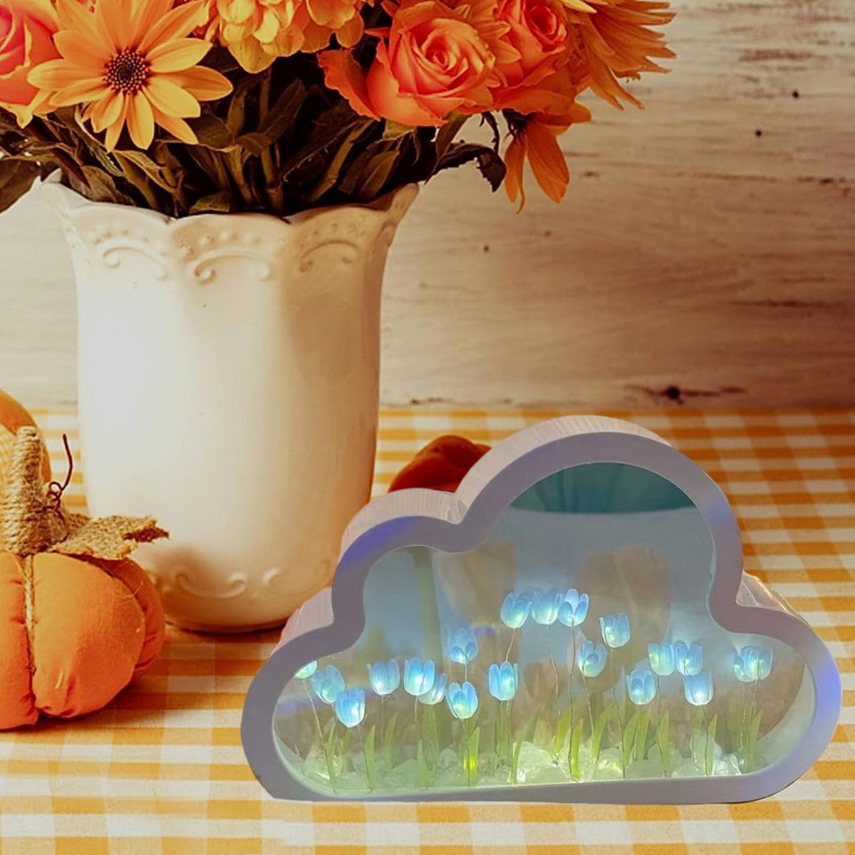 Wolkenförmiges Licht mit blauen Tulpen und eine Vase mit orangefarbenen Blumen auf einem Tisch.