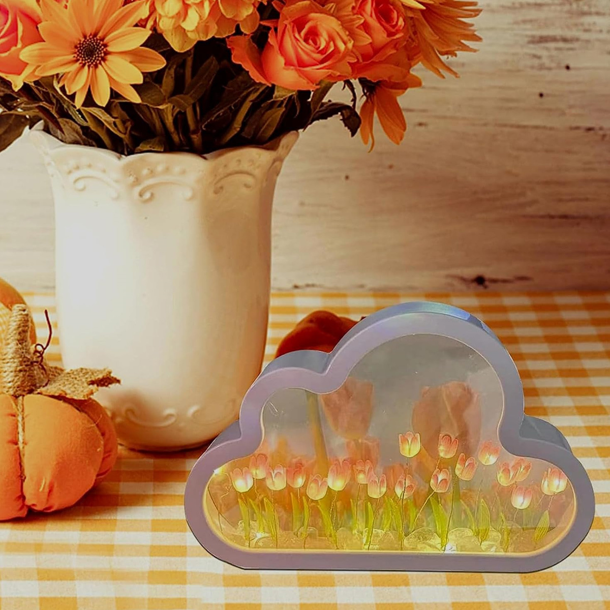 Wolkenförmige Lampe mit Blumen, umgeben von einer weißen Blumenvase und Kürbissen.