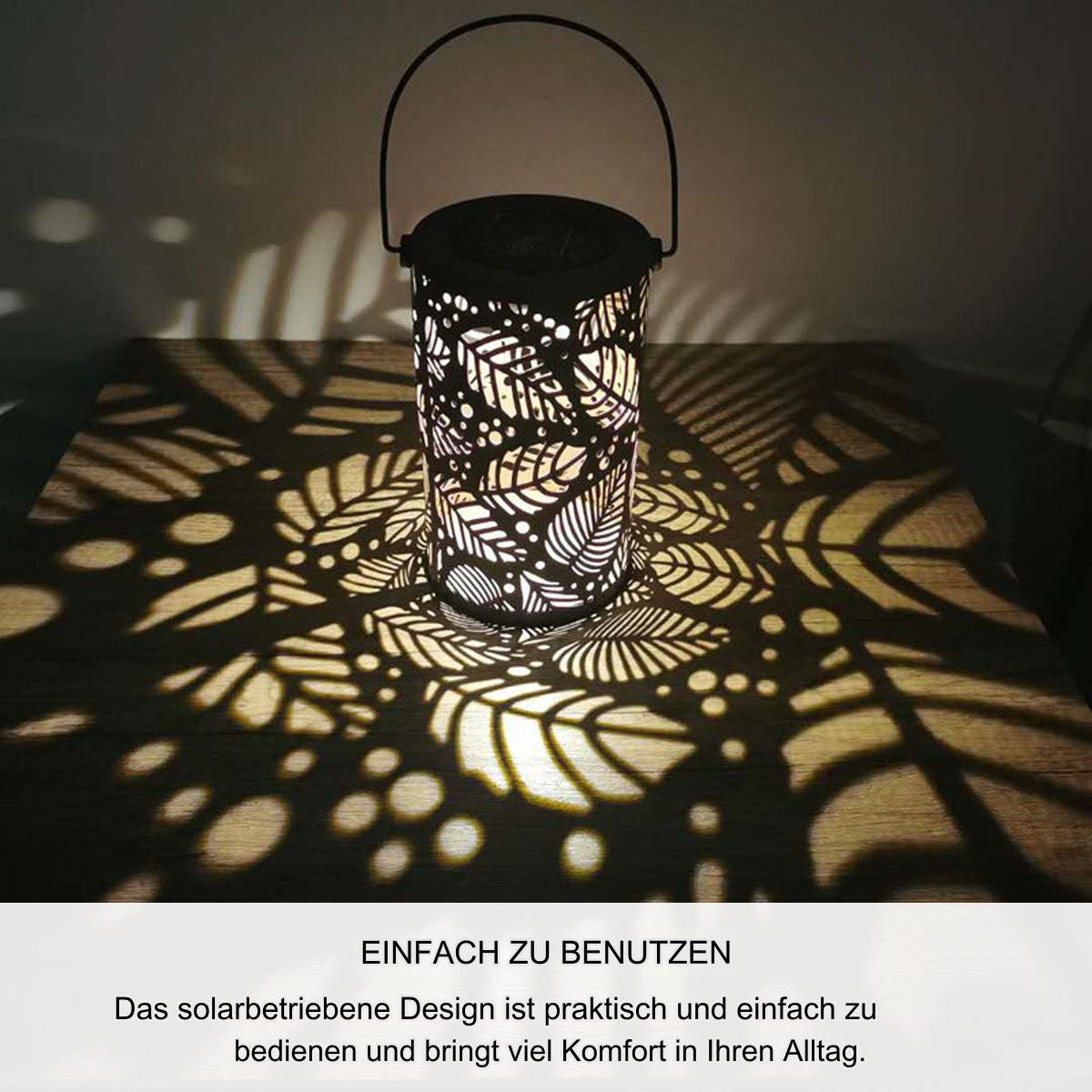 Beleuchtete Solar-Laterne mit Blattausschnitten, die Lichtmuster auf eine Holzoberfläche werfen.