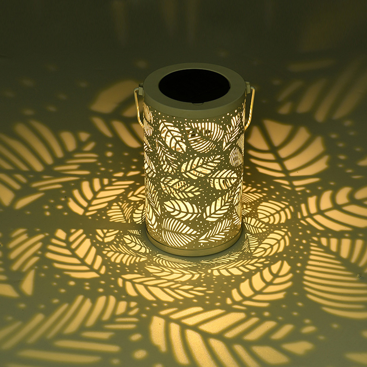 Zylindrische Laterne mit Blättermuster, wirft blattförmige Schatten auf den Boden.